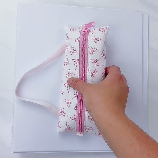 Beginner-friendly sewing pattern for a pink zippered pencil pouch with elastic, shown wrapped around school notebooks and a binder—perfect back-to-school supply case for pens, markers, and glue stick, aloha sewing company, bookmark, sewing tutorial video